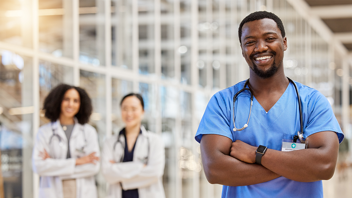 Male nurse standing in front of hospital smiling 