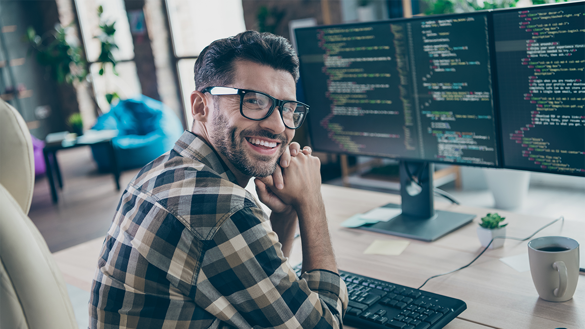Web and Digital Interface Designer sitting in front of computer, smiling at the camera